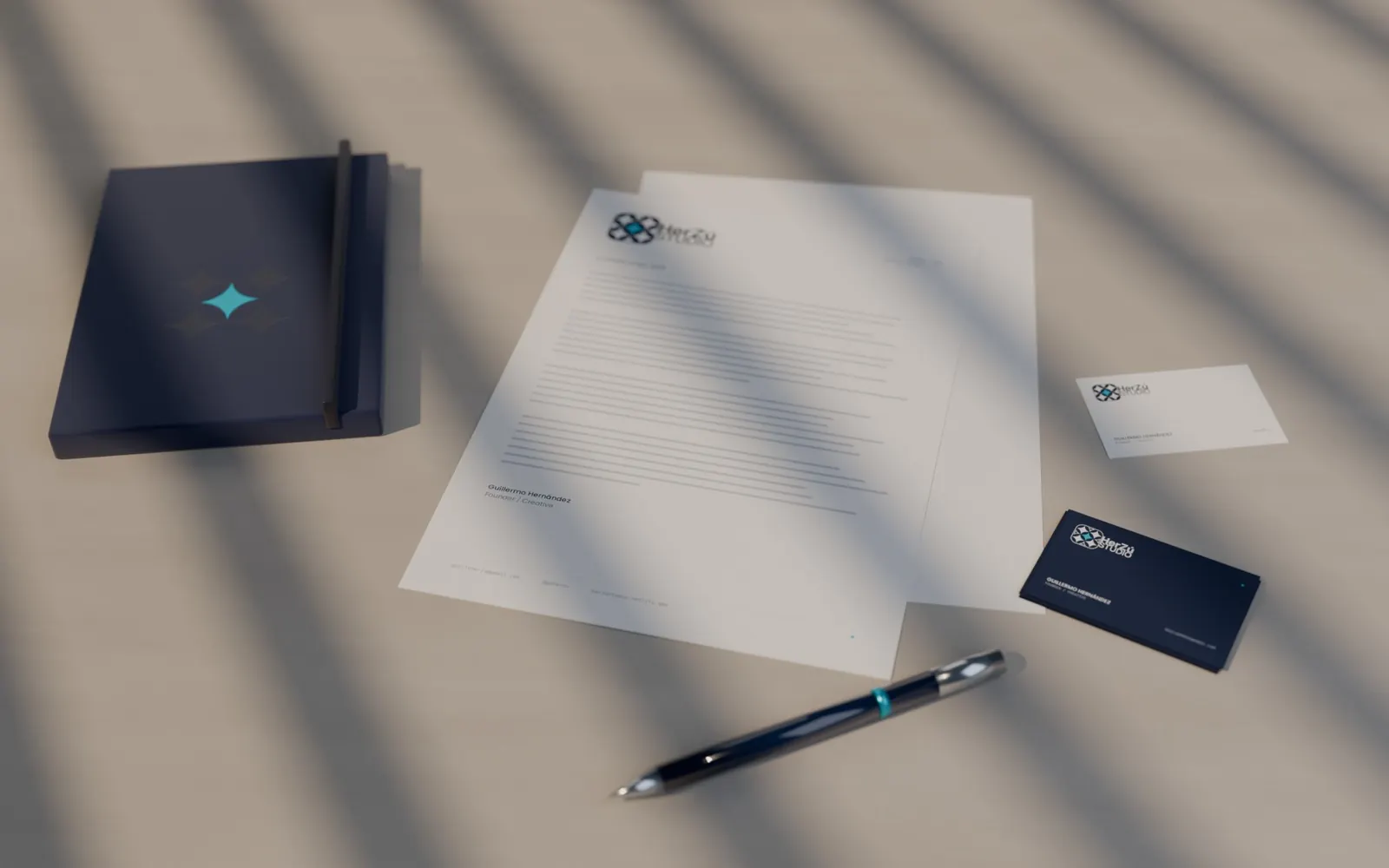 Render of HerZú Studio stationery on a stone table in striped window light: navy notebook with a debossed symbol, letterhead, business cards and a navy pen.